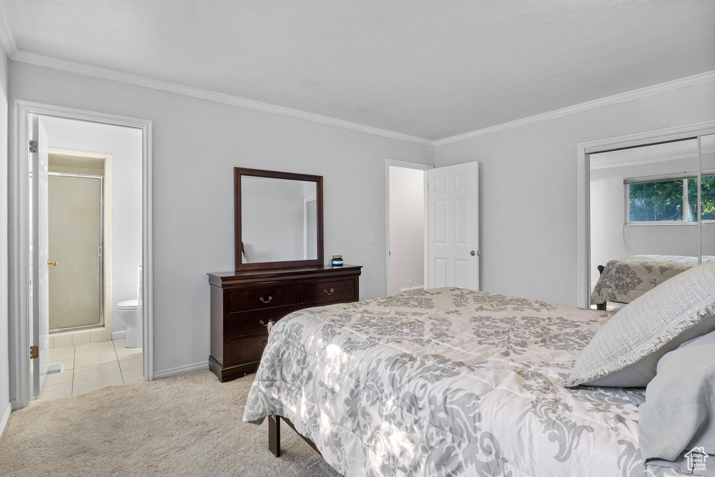Bedroom featuring ornamental molding, light colored carpet, ensuite bath, a closet, and light tile patterned floors