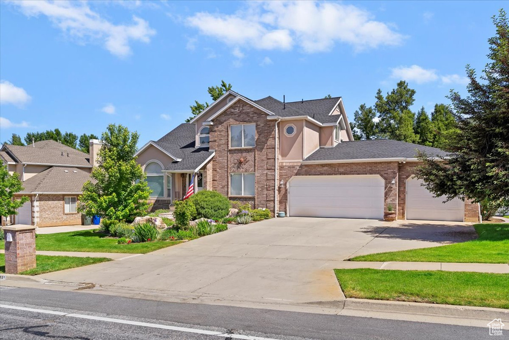 Traditional-style home with an attached garage, driveway, brick siding, a shingled roof, and a front lawn
