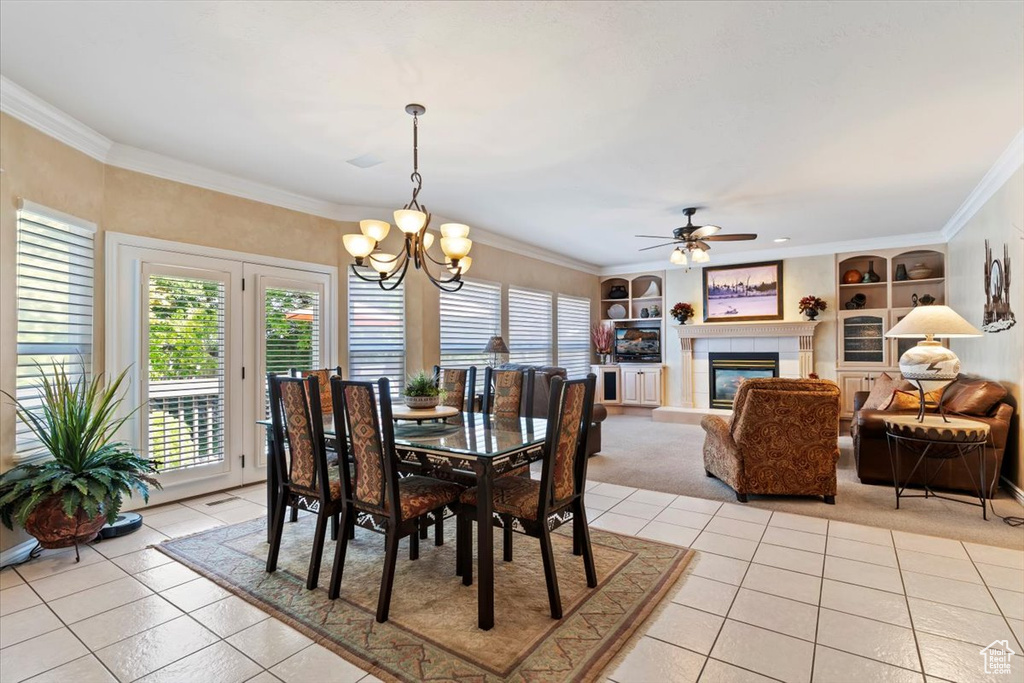 Dining area featuring light tile patterned flooring, built in features, a ceiling fan, a chandelier, and ornamental molding