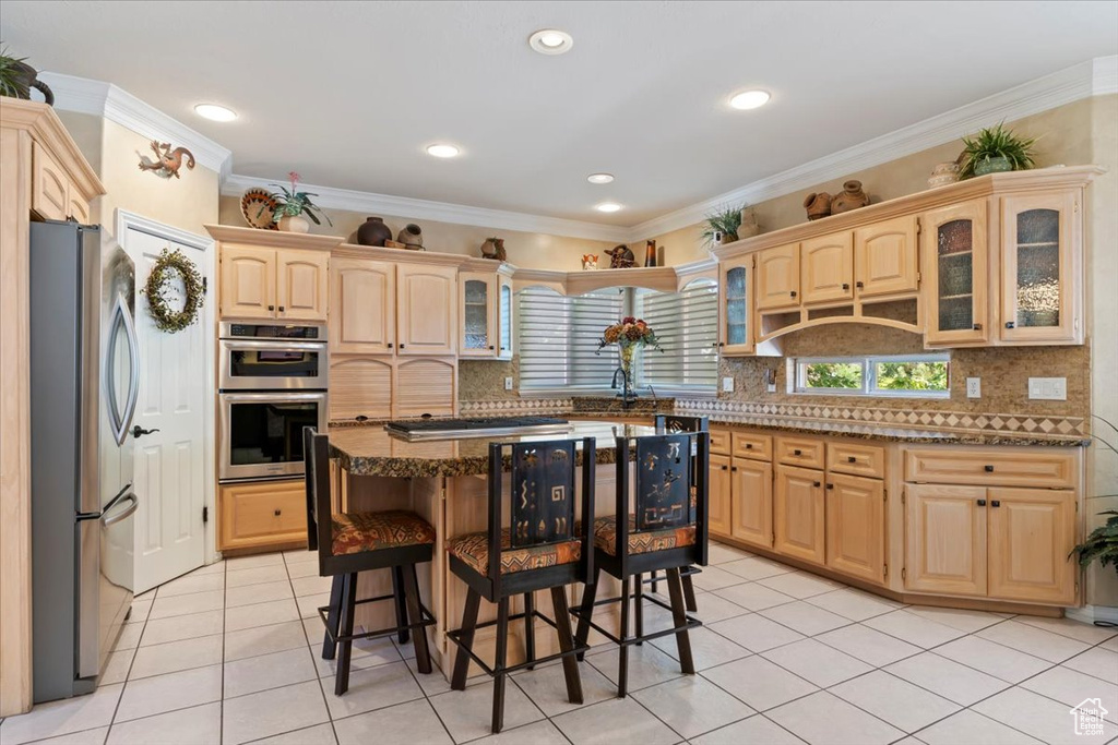 Kitchen featuring appliances with stainless steel finishes, dark stone countertops, light brown cabinets, a kitchen bar, and light tile patterned floors