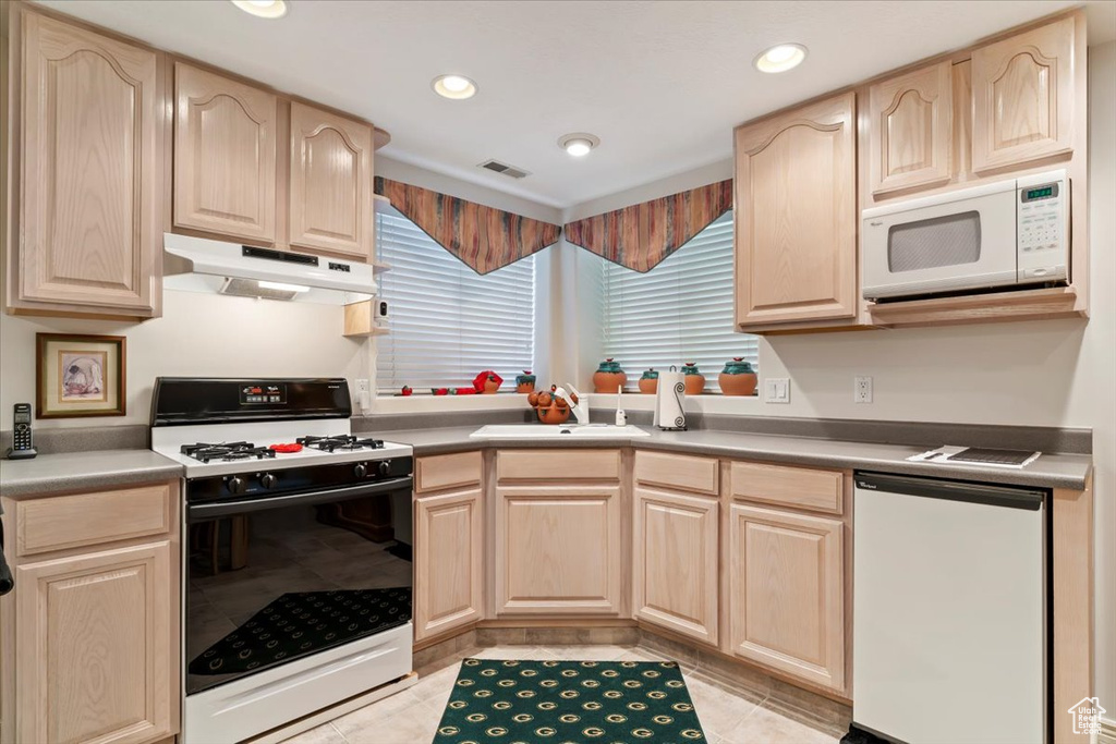 Kitchen with white appliances, under cabinet range hood, light brown cabinets, recessed lighting, and light tile patterned floors