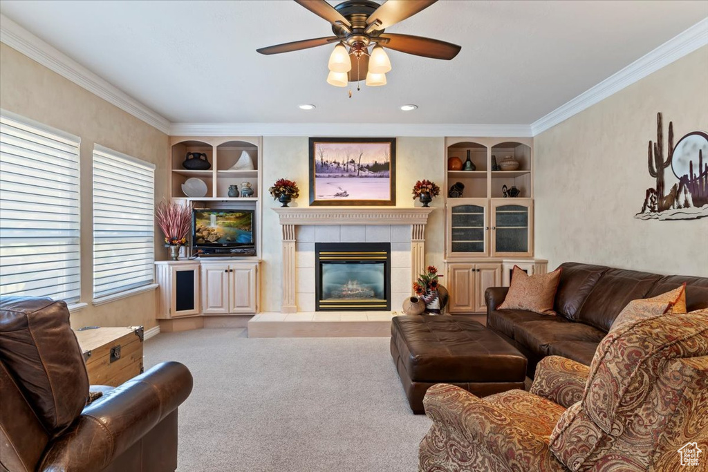 Living area featuring built in features, crown molding, a ceiling fan, a fireplace, and carpet floors