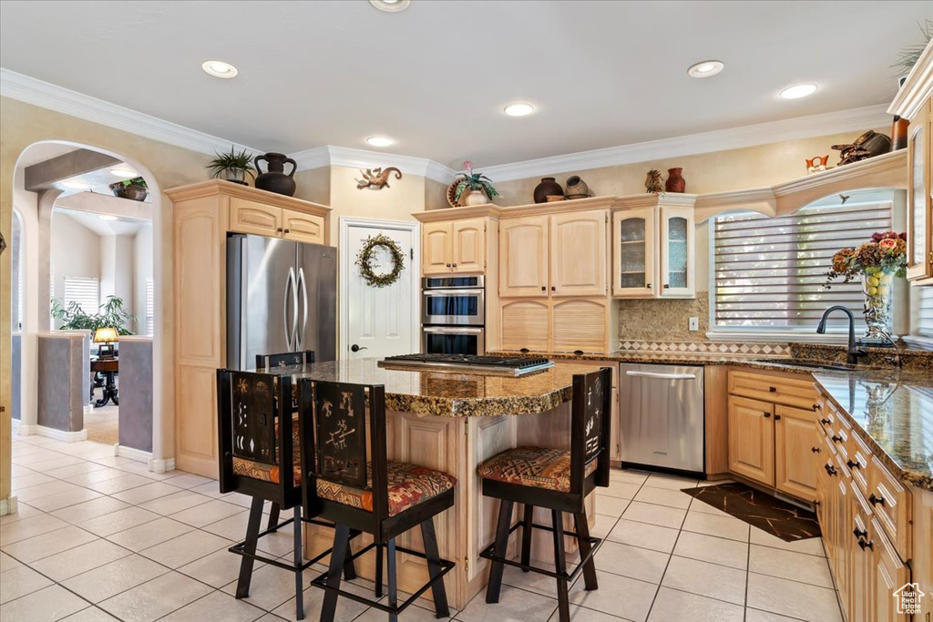 Kitchen featuring stainless steel appliances, light tile patterned flooring, a kitchen bar, a kitchen island, and light brown cabinetry