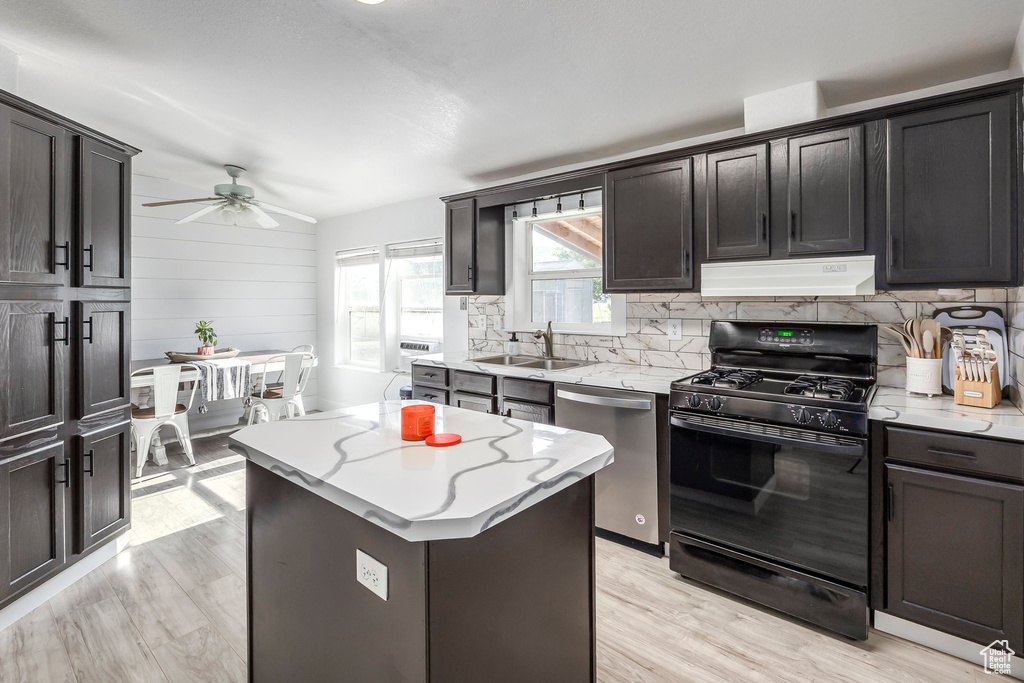 Kitchen with black range with gas stovetop, dishwasher, under cabinet range hood, a ceiling fan, and tasteful backsplash