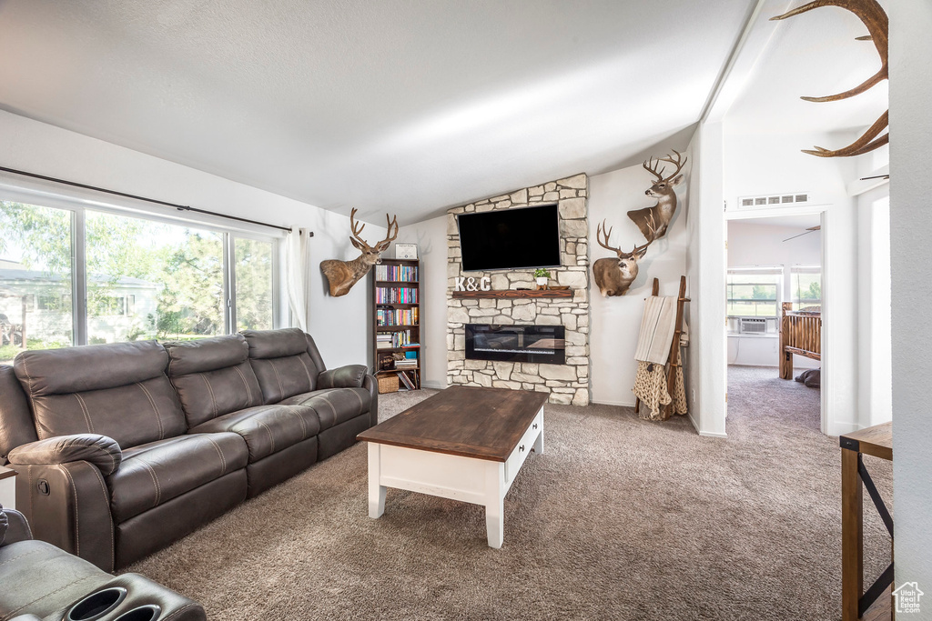 Carpeted living area featuring lofted ceiling, plenty of natural light, a fireplace, and cooling unit