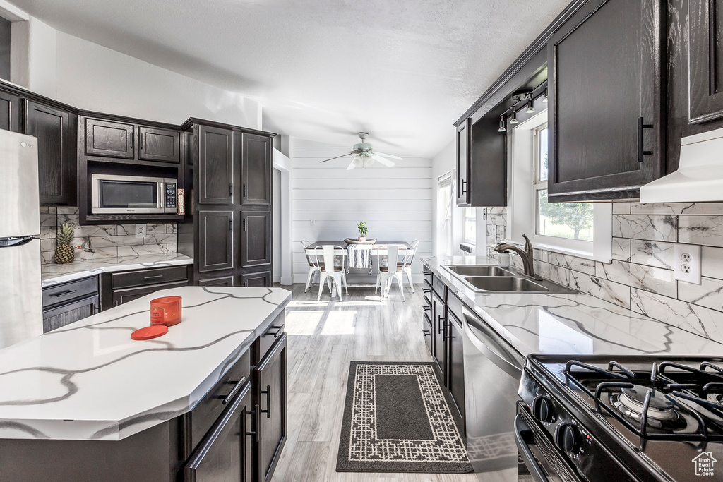 Kitchen featuring stainless steel appliances, decorative backsplash, a ceiling fan, light wood-type flooring, and light stone countertops