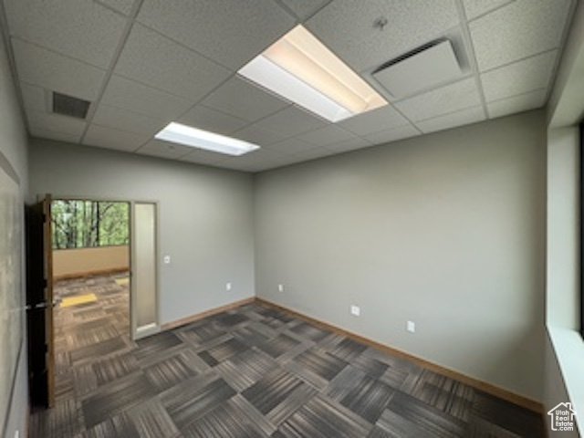 Unfurnished room with a drop ceiling and dark carpet