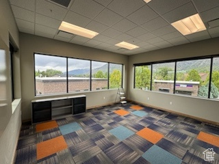 Spare room featuring healthy amount of natural light, a paneled ceiling, and dark colored carpet