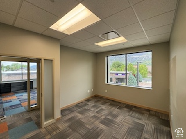 Carpeted empty room featuring a paneled ceiling and baseboards