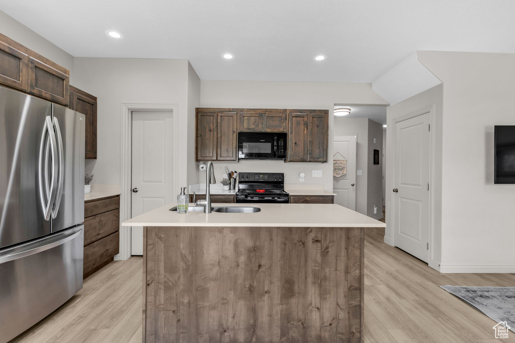 Kitchen with black appliances, light wood-style flooring, light countertops, a kitchen island with sink, and recessed lighting
