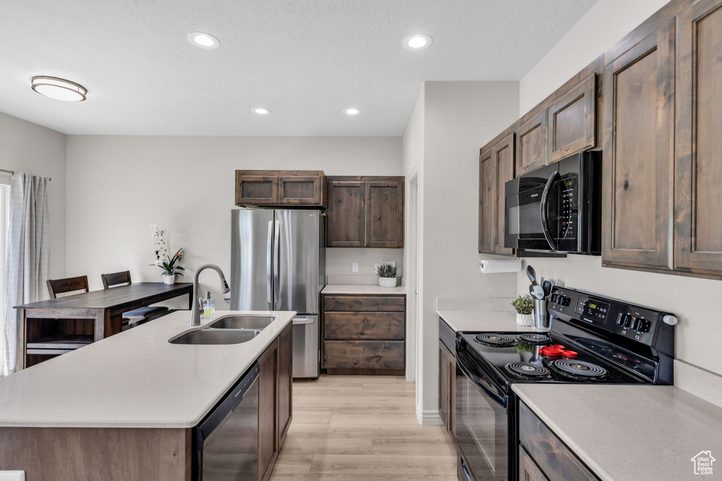 Kitchen featuring black appliances, light wood-type flooring, light countertops, recessed lighting, and a kitchen island with sink