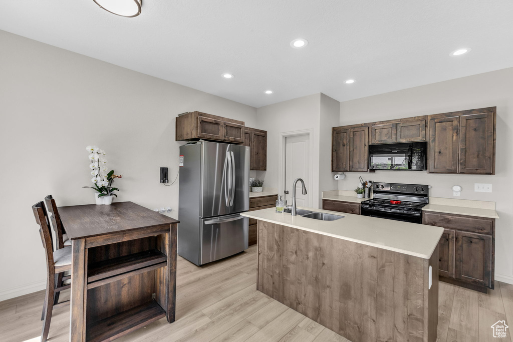 Kitchen with black appliances, light wood-type flooring, dark brown cabinetry, a kitchen island with sink, and recessed lighting