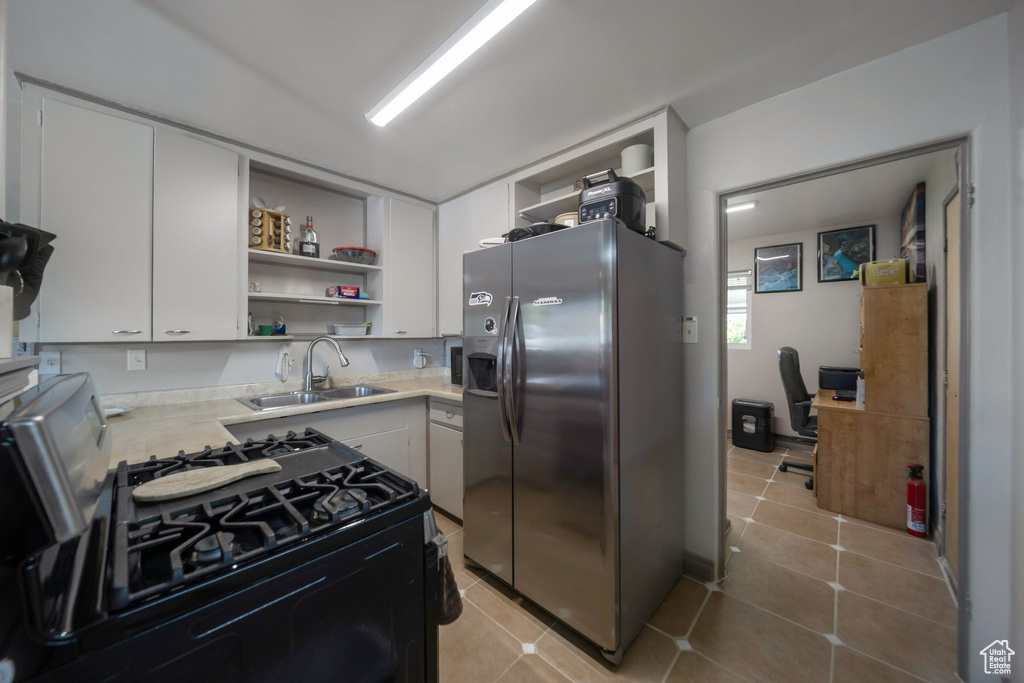 Kitchen with stainless steel refrigerator with ice dispenser, open shelves, gas range oven, light countertops, and white cabinetry