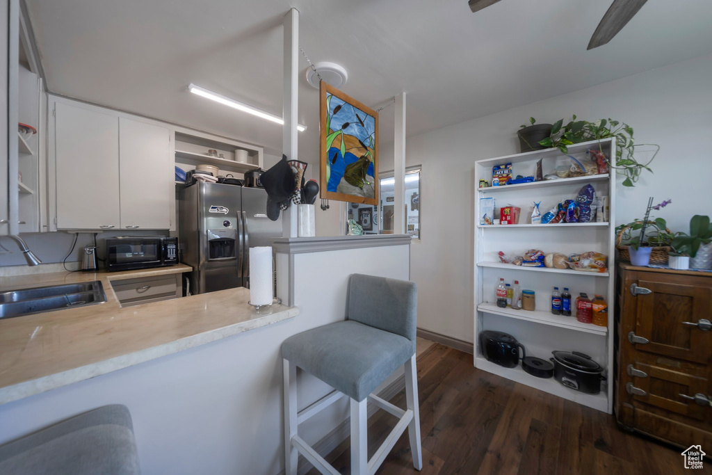 Kitchen featuring stainless steel refrigerator with ice dispenser, open shelves, black microwave, white cabinetry, and dark wood finished floors