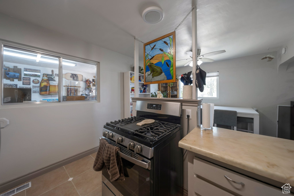 Kitchen with gas range, light countertops, ceiling fan, light tile patterned flooring, and white cabinets