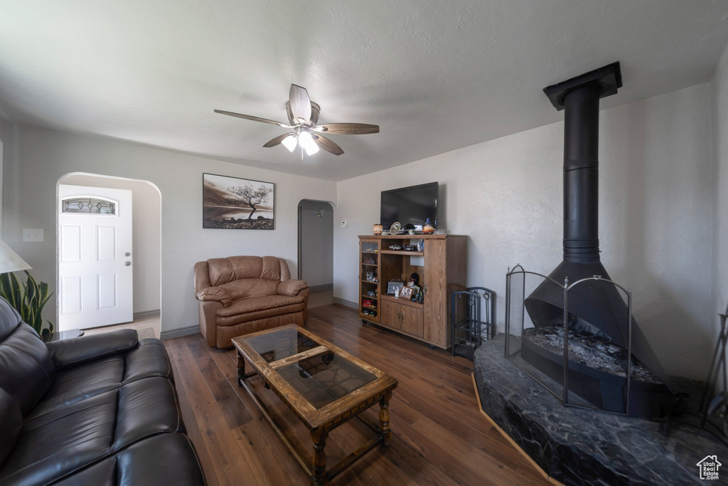 Living area with arched walkways, wood finished floors, a ceiling fan, and a wood stove