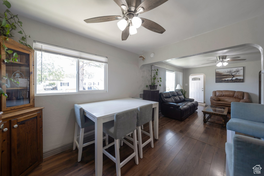 Dining space with arched walkways, a ceiling fan, and dark wood-style flooring