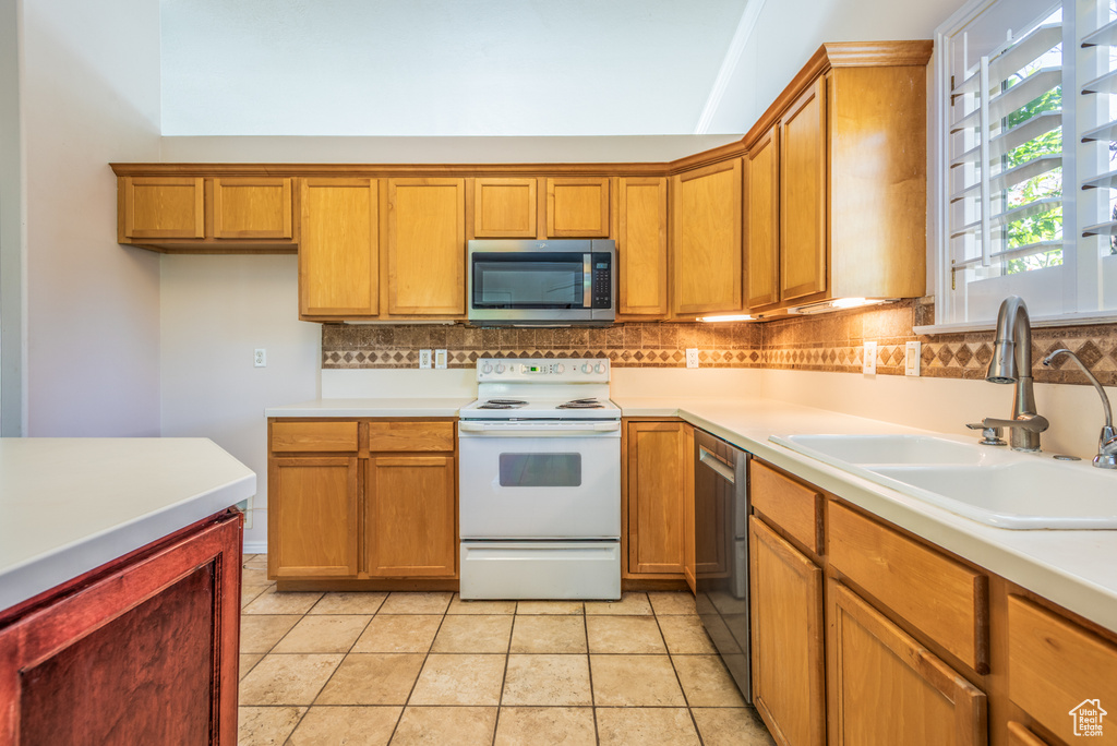 Kitchen with stainless steel appliances, brown cabinets, decorative backsplash, and light countertops
