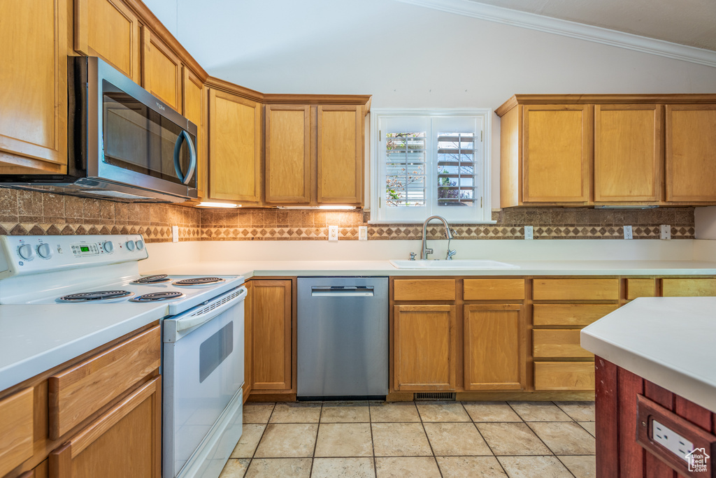 Kitchen featuring appliances with stainless steel finishes, lofted ceiling, decorative backsplash, ornamental molding, and light countertops