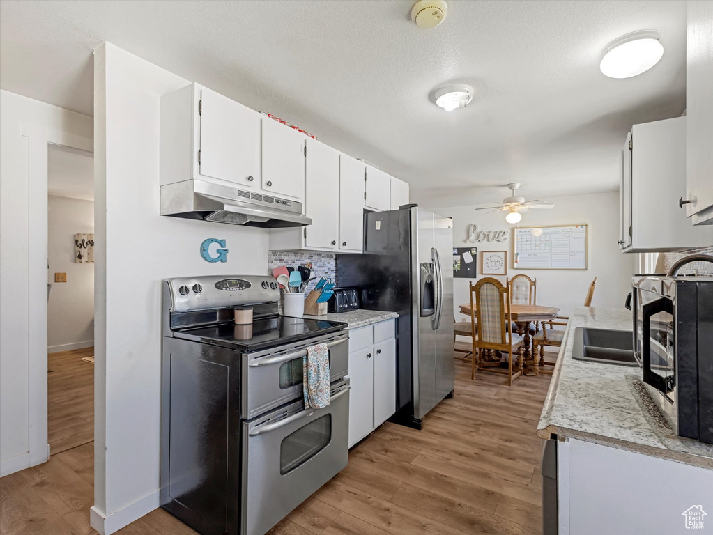 Kitchen with stainless steel appliances, under cabinet range hood, ceiling fan, light countertops, and light wood-type flooring