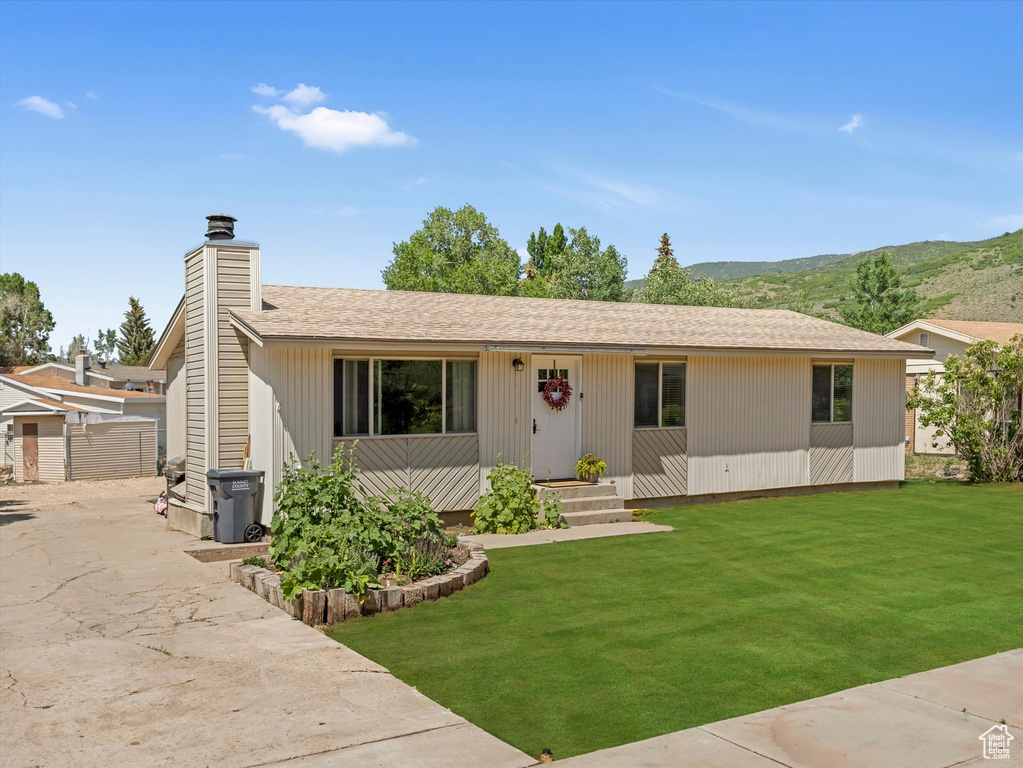 Single story home featuring a front lawn, a mountain view, a chimney, and roof with shingles