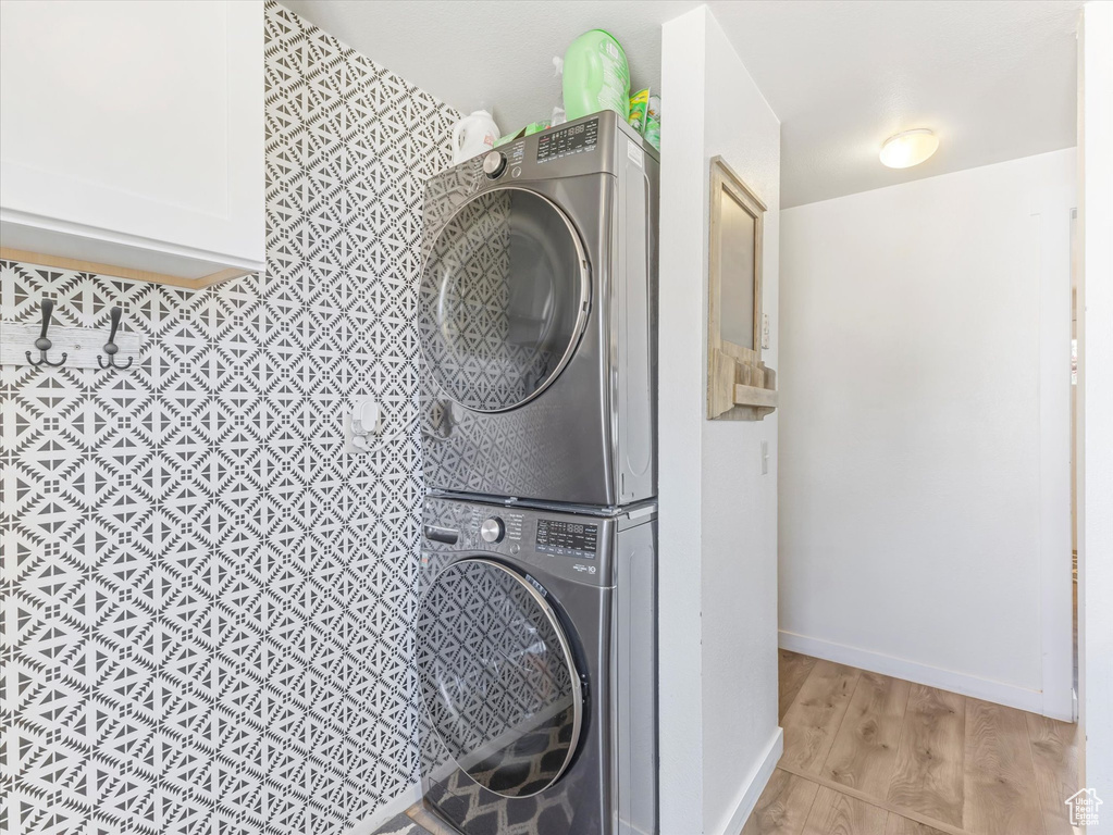 Laundry room with stacked washer / drying machine and light wood-style flooring