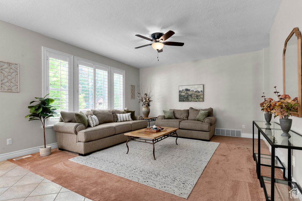 Living area featuring ceiling fan, light colored carpet, a textured ceiling, and light tile patterned floors