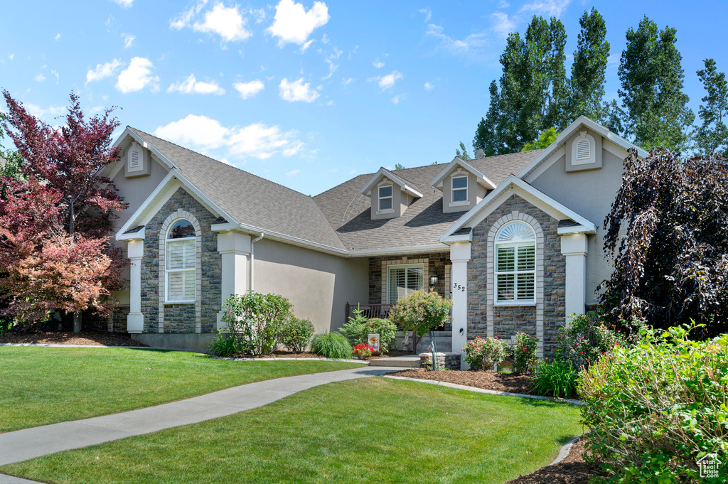 Traditional home with stone siding, stucco siding, a front lawn, and roof with shingles
