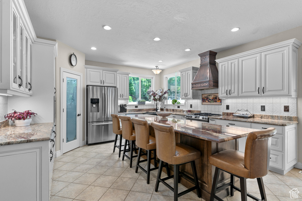 Kitchen with stainless steel refrigerator with ice dispenser, custom range hood, decorative backsplash, a breakfast bar, and a center island