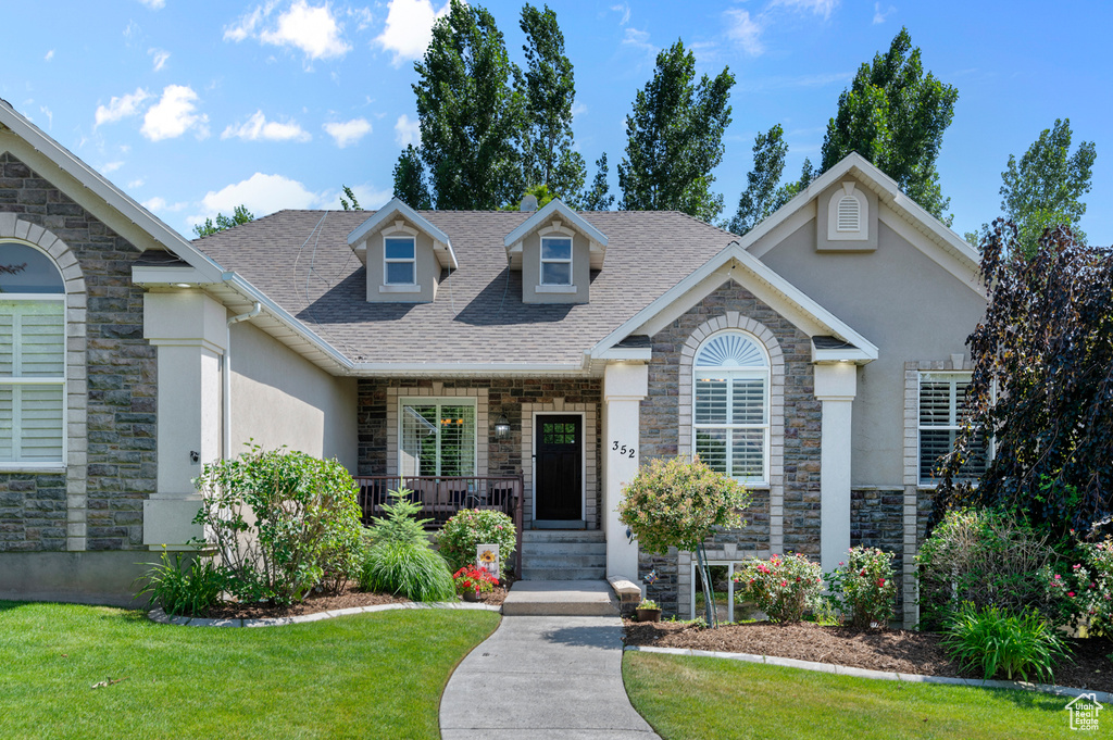 View of front of home with stone siding, a front yard, a shingled roof, and stucco siding