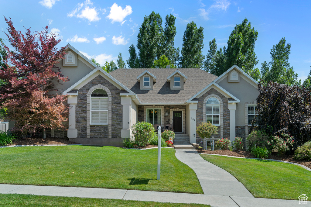 View of front facade with stone siding, a front lawn, and stucco siding