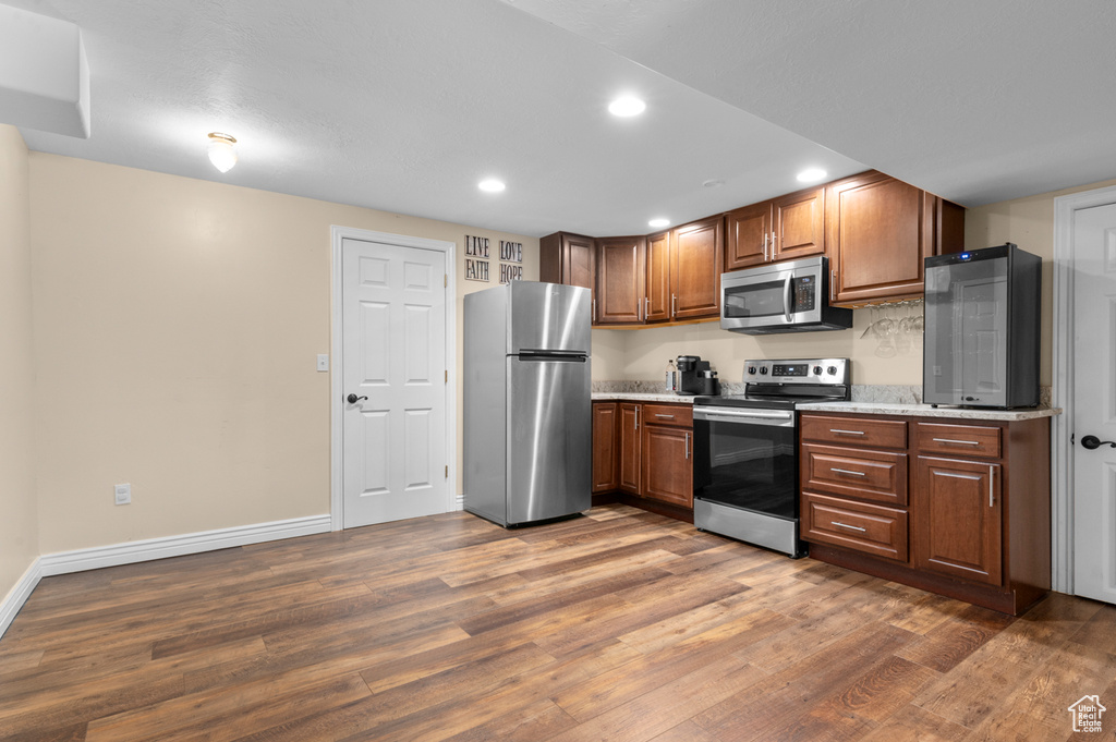 Kitchen featuring appliances with stainless steel finishes, wood finished floors, recessed lighting, brown cabinetry, and light stone countertops