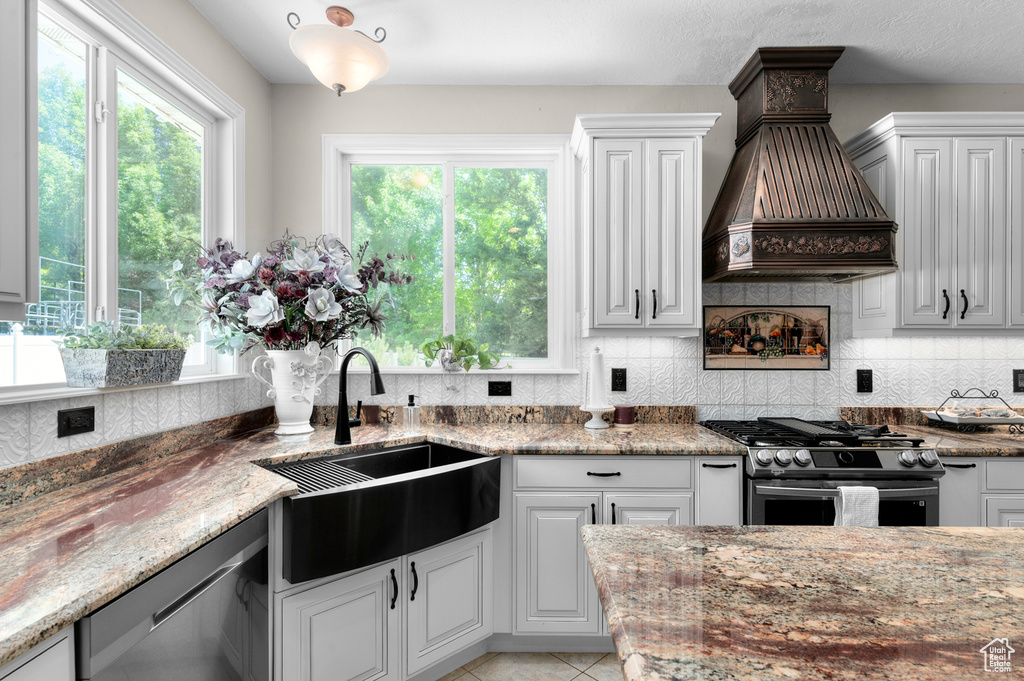 Kitchen with stainless steel appliances, premium range hood, plenty of natural light, and backsplash