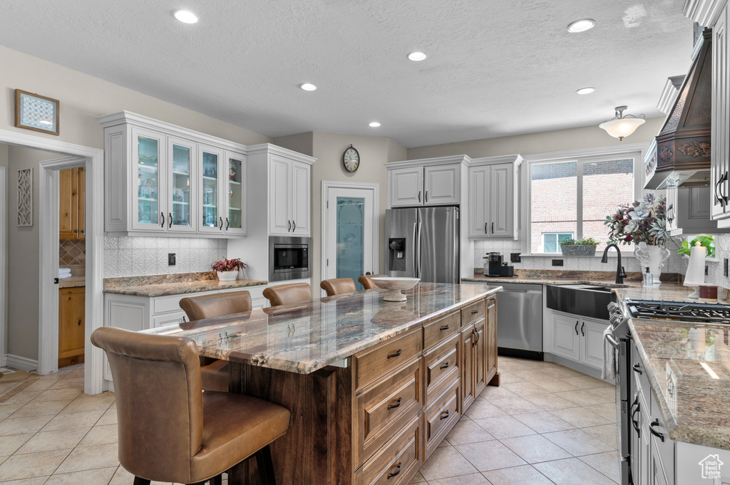 Kitchen with appliances with stainless steel finishes, a breakfast bar, a center island, light tile patterned floors, and backsplash