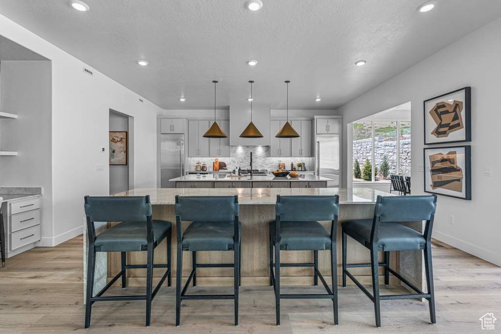 Kitchen featuring a large island, built in refrigerator, decorative backsplash, recessed lighting, and light wood-style flooring