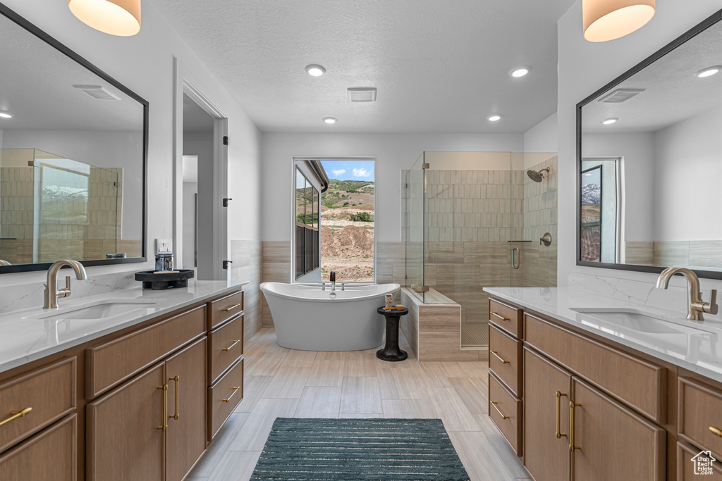 Full bathroom featuring two vanities, a stall shower, a freestanding tub, and recessed lighting