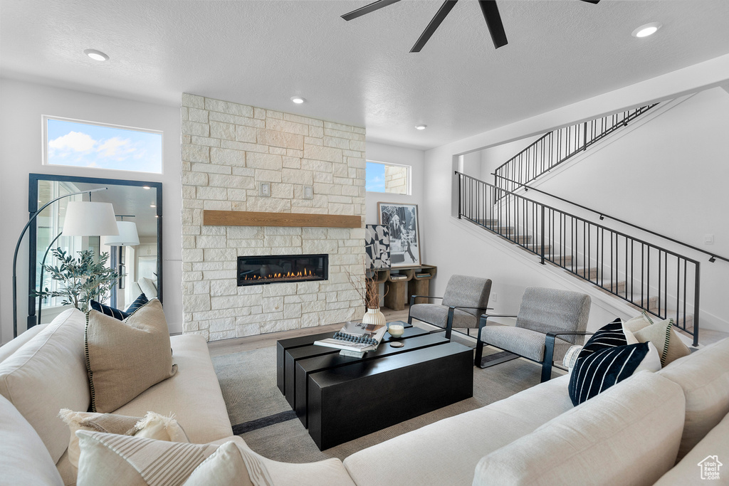 Living area featuring ceiling fan, stairs, a textured ceiling, recessed lighting, and a stone fireplace