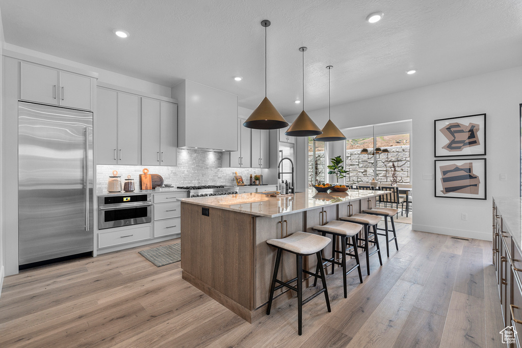 Kitchen with appliances with stainless steel finishes, light wood-type flooring, a breakfast bar, backsplash, and light stone countertops