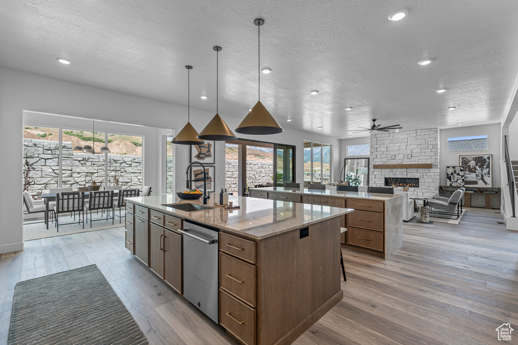 Kitchen with a large island with sink, a stone fireplace, dishwasher, a textured ceiling, and light wood-style floors