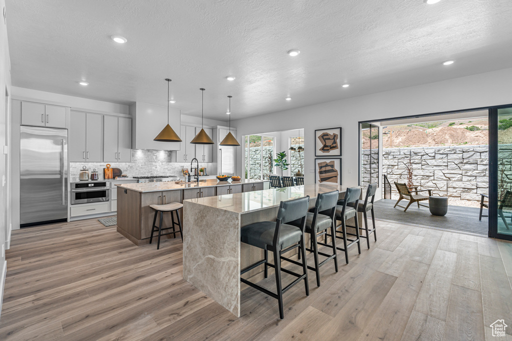 Kitchen featuring stainless steel appliances, a spacious island, recessed lighting, a kitchen bar, and light wood finished floors