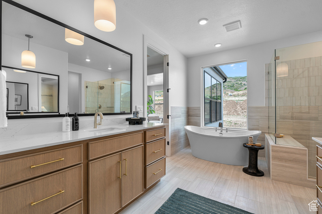 Full bathroom with tile walls, vanity, a stall shower, a freestanding bath, and wainscoting