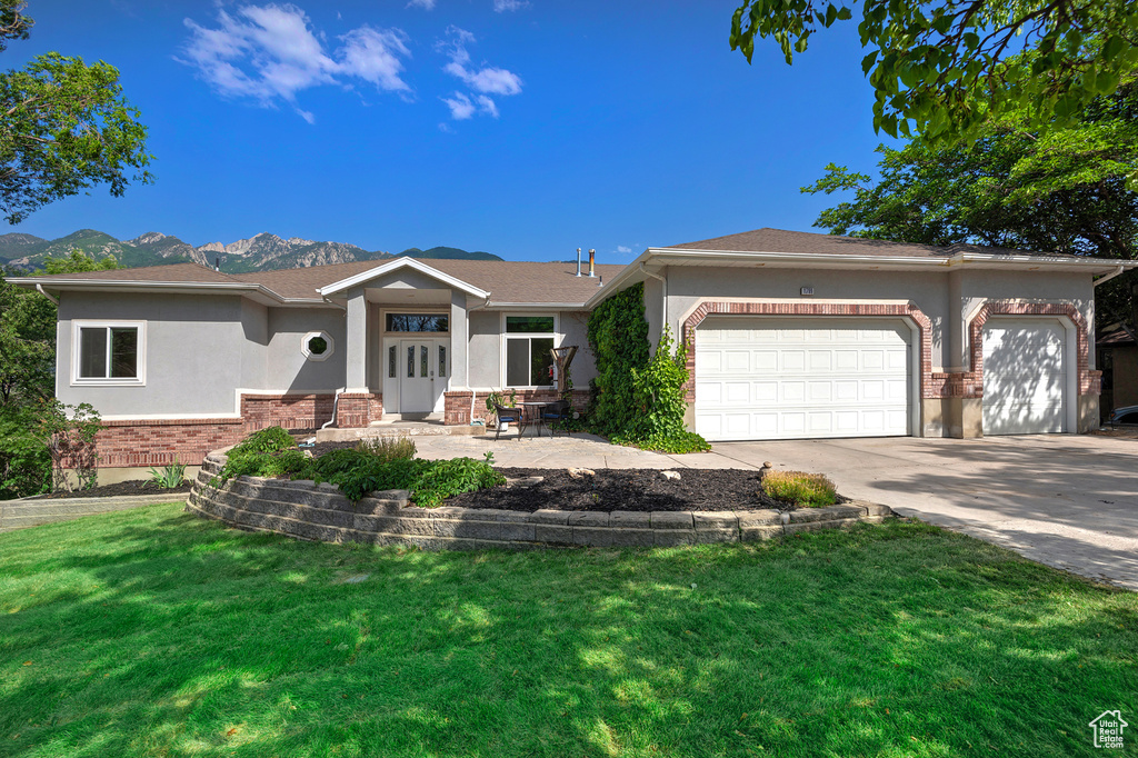 View of front of property featuring stucco siding, an attached garage, a front lawn, concrete driveway, and a mountain view