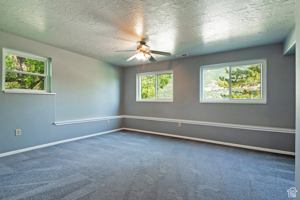 Empty room with a ceiling fan, carpet floors, and a textured ceiling
