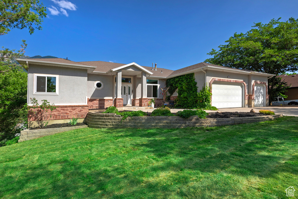 View of front of home featuring stucco siding, an attached garage, brick siding, and a front yard