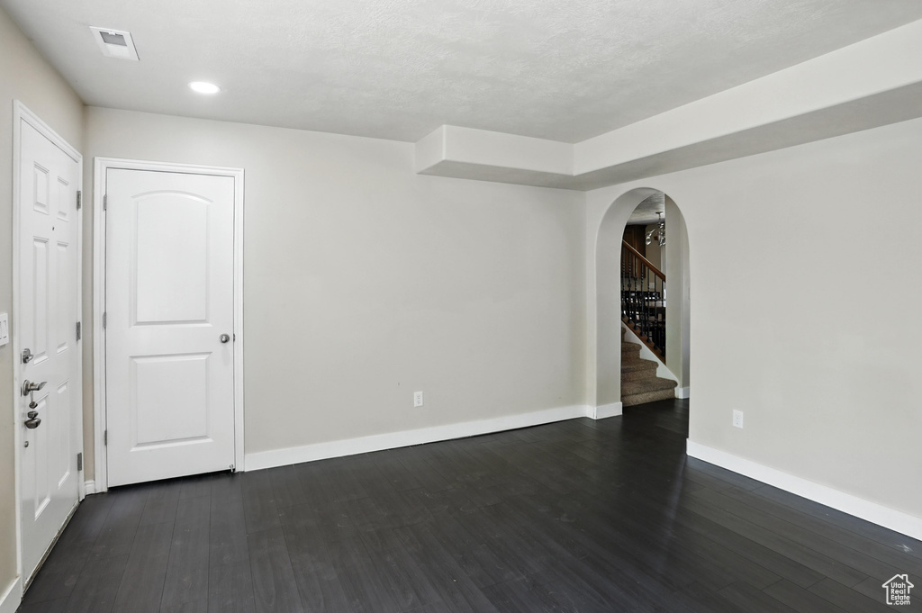 Empty room with arched walkways, dark wood finished floors, stairway, and recessed lighting