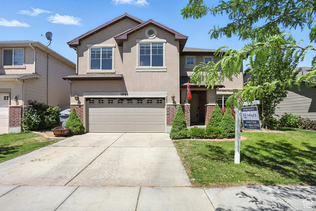 Traditional home featuring stucco siding, a garage, a front lawn, driveway, and brick siding