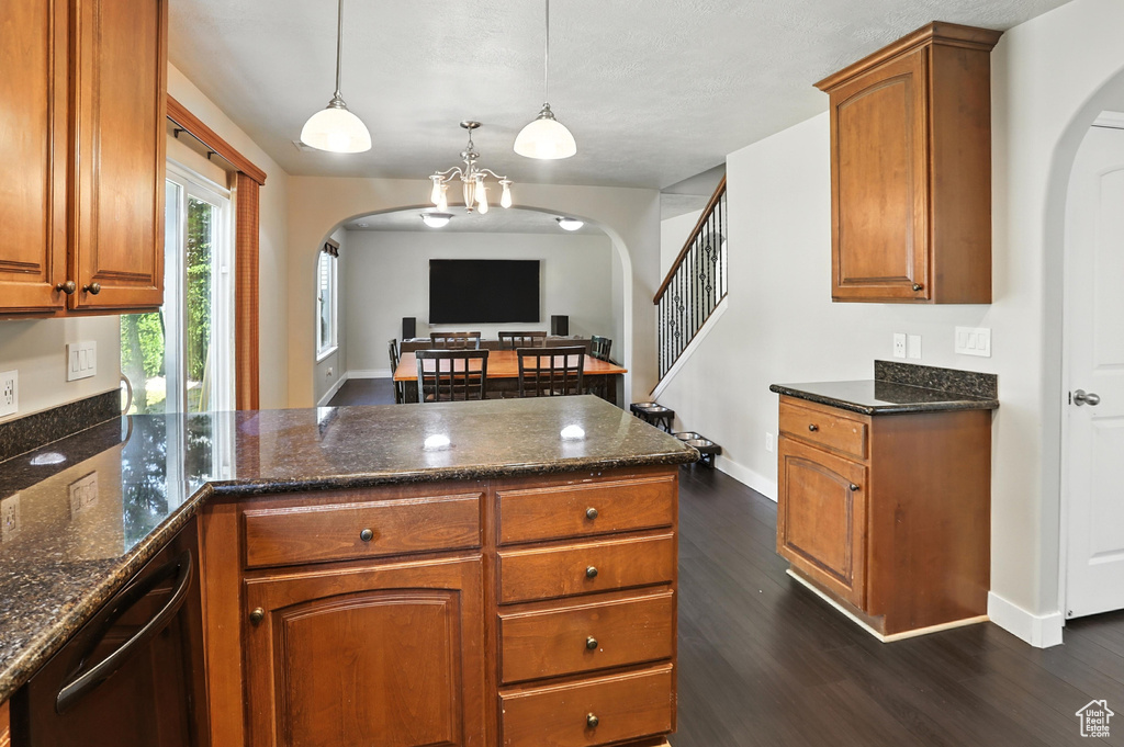 Kitchen featuring arched walkways, a peninsula, dark wood-style floors, brown cabinetry, and dark stone counters