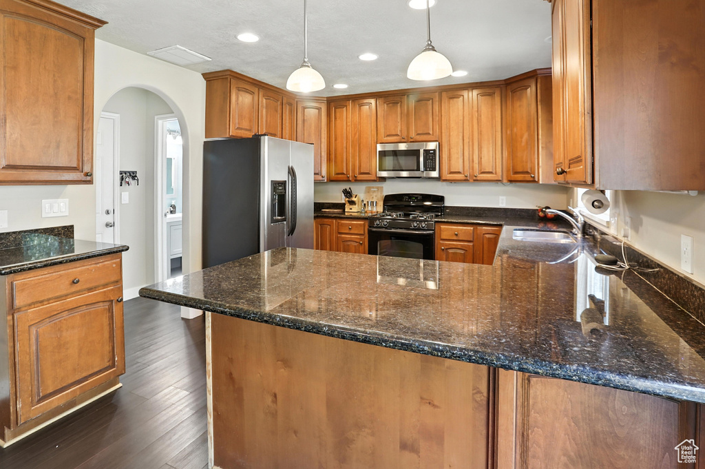 Kitchen featuring appliances with stainless steel finishes, a peninsula, recessed lighting, arched walkways, and brown cabinets