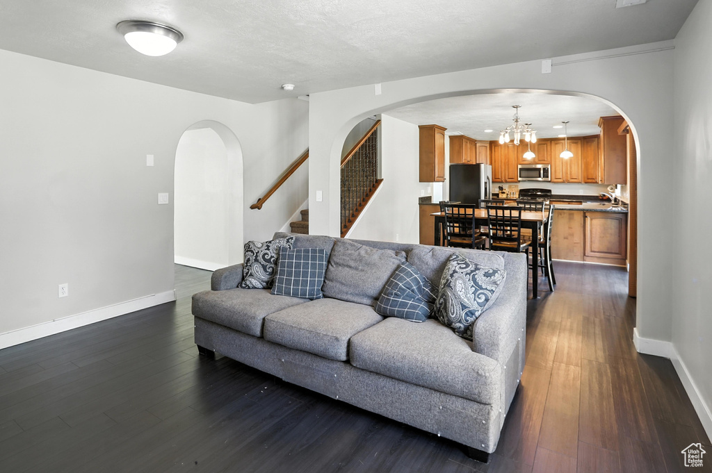 Living area featuring arched walkways, a chandelier, dark wood-style floors, and stairs
