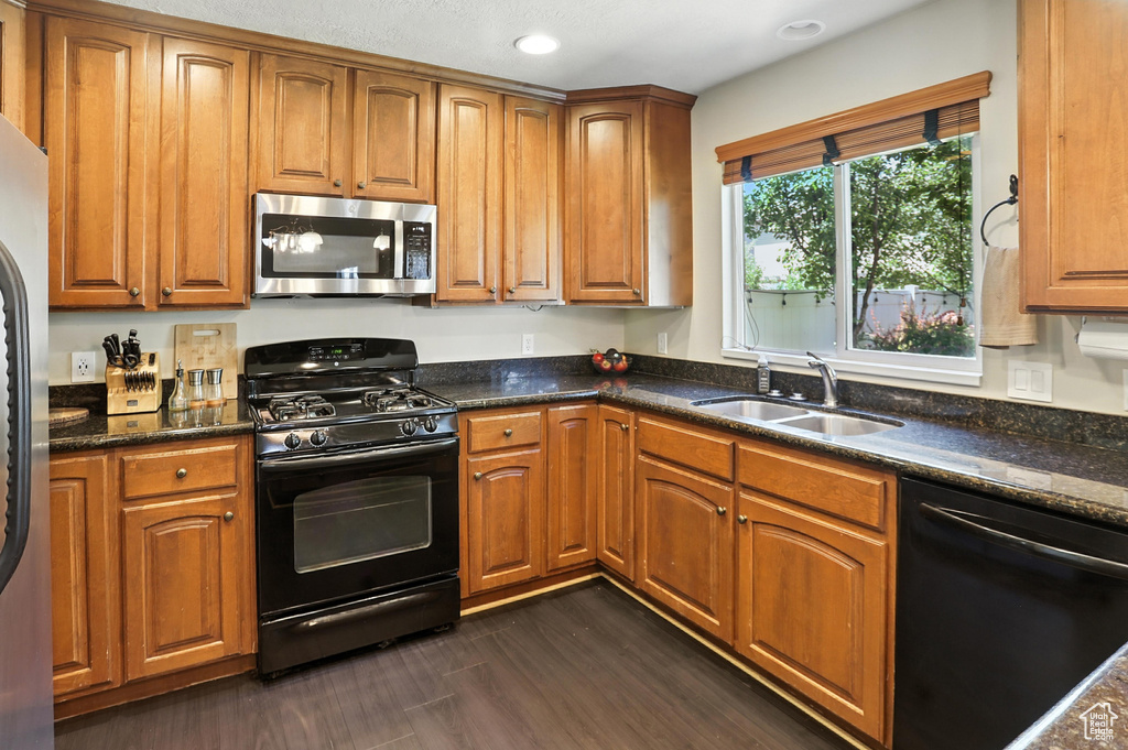 Kitchen with black appliances, brown cabinetry, dark stone countertops, and recessed lighting